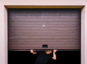 Man lifting brown garage door from inside.