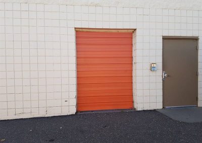 Orange commercial roll-up door beside entrance.